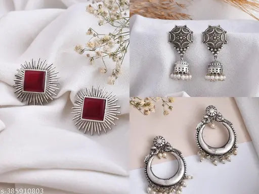 A set of three oxidized silver earrings, featuring a traditional jhumki, a red designer stud for a pop of color, and an ethnic chandbali. A diverse combo for stylish versatility